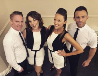 Four performers dressed in black and white posing backstage