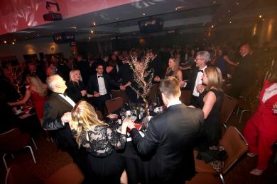 Corporate black tie event with all guests on their feet linked around their tables during our surprise entertainment show