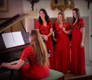 Christmas themed entertainment from The Noelles UK, four girls in red gowns around a grand piano