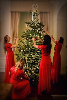 The Noelles UK four piece in red gowns dressing a Christmas tree